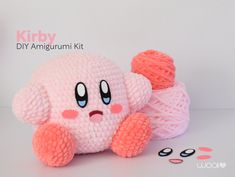 a pink stuffed animal sitting next to two balls of yarn