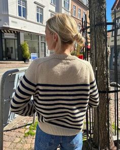 a woman standing next to a tree wearing a sweater