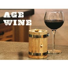 a glass of wine next to a wooden barrel on a table with the words age wine written above it