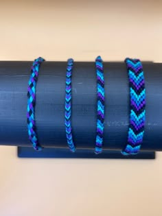 four different colored bracelets sitting on top of a blue piece of metal pipe with one knot in the middle