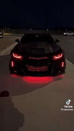 the back end of a black sports car with its lights turned on at night time