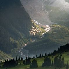 the mountains are covered in green grass and trees, with a river running through them