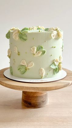 a green cake with white flowers on it sitting on top of a wooden table next to a plate