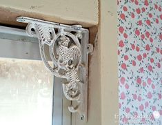 the corner of a window with an ornate iron frame and flowered wall paper behind it