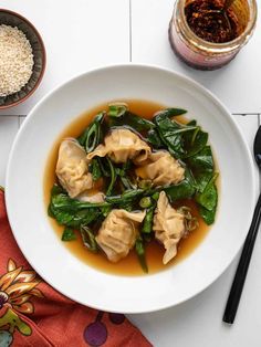 a white plate topped with dumplings covered in broth next to a bowl of rice