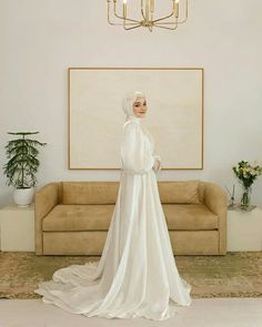 a woman standing in front of a couch wearing a white dress and head scarf with her hands on her hips