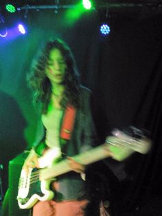 a woman with long hair playing an electric guitar in front of green and blue lights