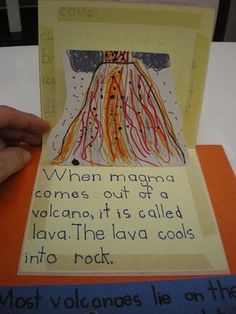 someone is holding up a piece of paper with an image of a volcano on it