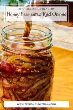 a jar filled with honey fermowed red onions on top of a wooden table