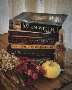 a stack of books sitting on top of a wooden table next to a vase filled with flowers