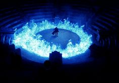 a man standing in the middle of a fire pit with blue flames on it's sides