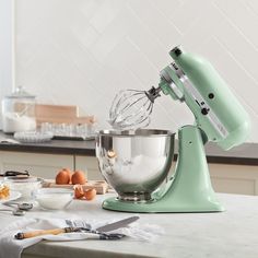 a green mixer sitting on top of a kitchen counter next to eggs and utensils