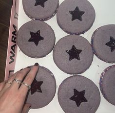 a hand is pointing at some cupcakes with stars on them in a box