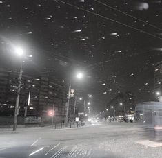 a city street at night with snow falling on the ground and buildings in the background