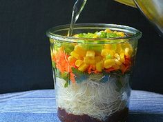 someone pouring dressing into a glass container filled with veggies and shredded white rice