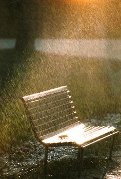 a park bench sitting in the middle of a field with water splashing on it