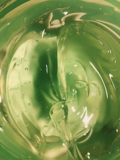 a green liquid swirls in the center of a glass bowl with water droplets on it