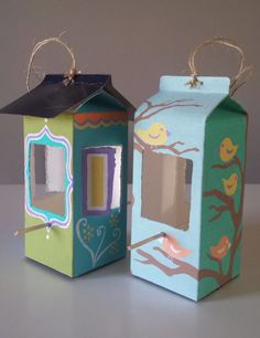 two boxes are decorated like houses with trees and birds painted on the sides, one has a candle in it