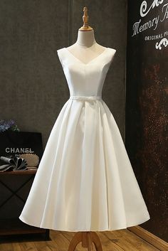 a white dress on a mannequin stand in front of a wall