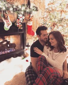 a man and woman sitting in front of a christmas tree