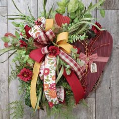 a heart - shaped wreath with ribbons and flowers on a wooden background is decorated with greenery