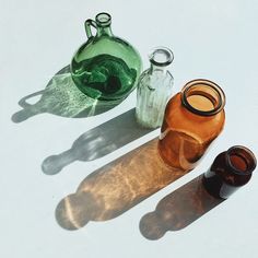 three glass bottles sitting next to each other on a white surface with shadows from them