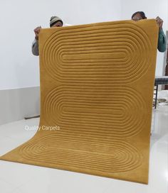 two men holding up a large rug in the middle of a room with white walls