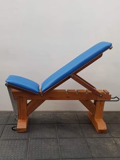 a wooden bench sitting on top of a tiled floor next to a white wall with a blue cushion