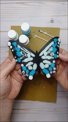 a person holding a butterfly with paint on it's wings and two small bottles next to it