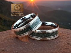 two men's wedding bands sitting on top of a rock with the sun setting in the background