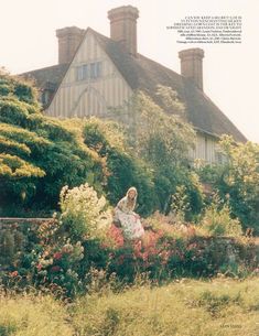 a woman sitting in the middle of a garden next to a building with two chimneys