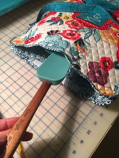 a person is holding a wooden mallet in front of a quilted pillow on a cutting board