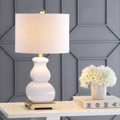 a white table lamp sitting on top of a book next to a vase with flowers