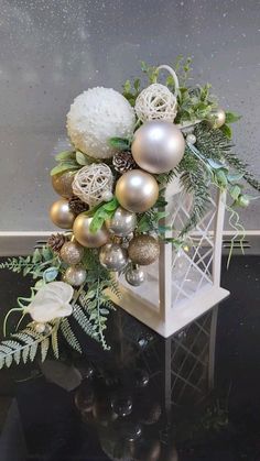 a white and gold christmas arrangement on a black table with silver balls, greenery and pine cones