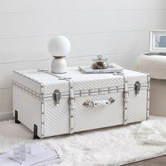 a white trunk sitting on top of a rug next to a chair and table with a lamp