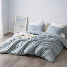 an unmade bed with blue comforter and pillows on the floor next to a painting