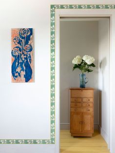 a vase with white flowers sitting on top of a wooden dresser next to a painting