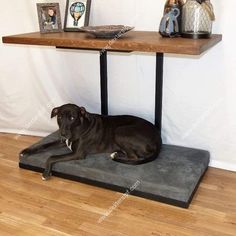 a large black dog laying on top of a mat under a table with pictures and vases