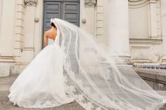 a woman in a wedding dress and veil is standing on the steps outside an old building