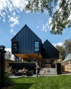 two people are sitting on the grass outside of a house with black metal sidings