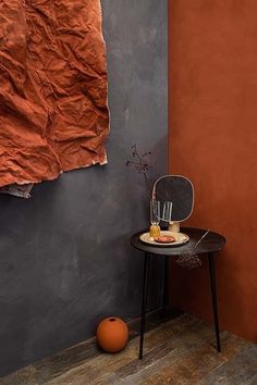 a chair sitting next to a table with an orange vase on it and a piece of paper hanging from the wall