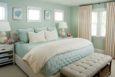 a bedroom with blue walls and white bedding, two windows and a bench in front of the bed