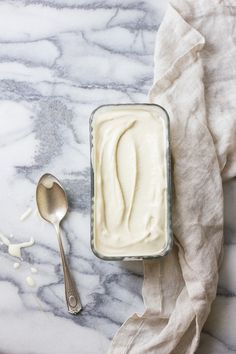 a bowl of yogurt next to a spoon on a marble counter top with white linen