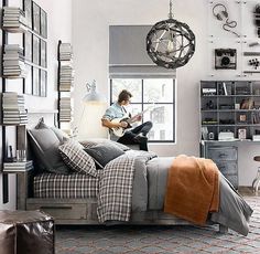 a man sitting on top of a bed in a bedroom next to a book shelf