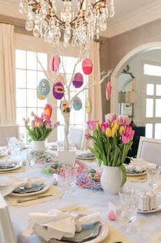 the table is set for easter dinner with tulips, eggs and other decorations