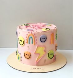 a pink birthday cake decorated with smiley faces and rainbows on the top is sitting on a plate