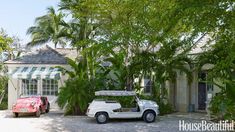 two cars parked in front of a house with palm trees and awnings on the roof