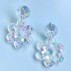 two pairs of white and multicolored earrings on a blue background with confetti sprinkles