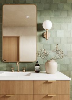 a bathroom vanity with a mirror, sink and vase on top of it in front of a green tiled wall