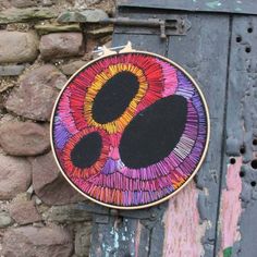 a colorful hand embroidered wall hanging on the side of a brick building next to a stone wall